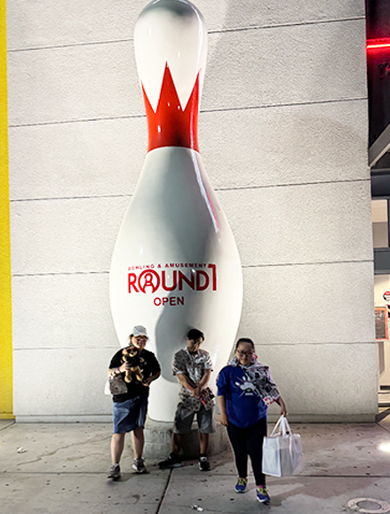 Three members outside a Round1 bowling and amusement centre, beside a giant bowling pin.