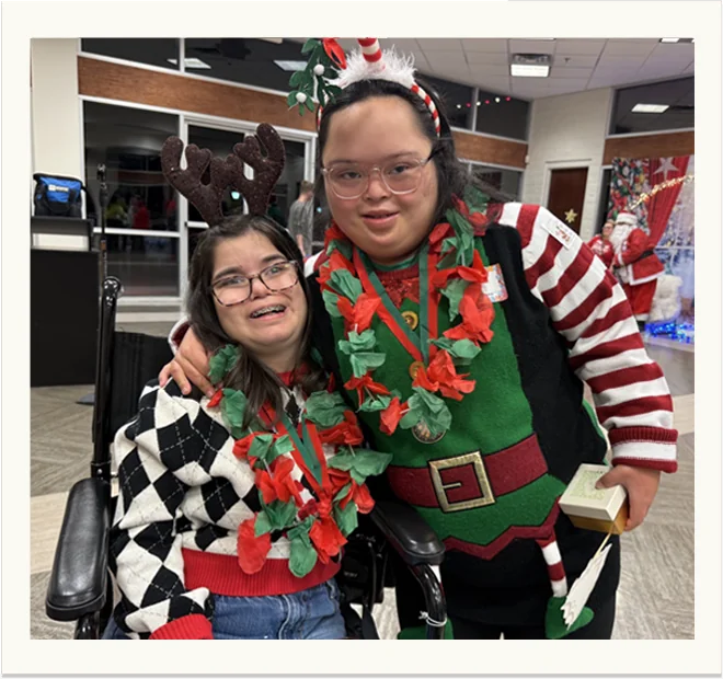 Two members in Christmas jumpers and antlers, arm in arm and laughing.