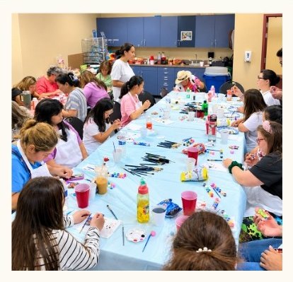 Members and families along a long table at an arts and crafts class, painting and decorating together.