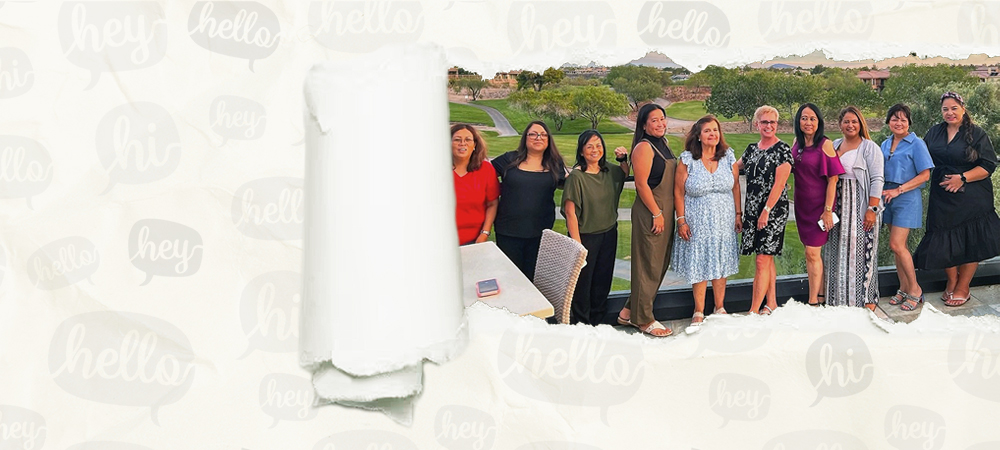 A group of women standing together on a terrace overlooking a golf course at sunset, seen through a tear in a sheet of paper.